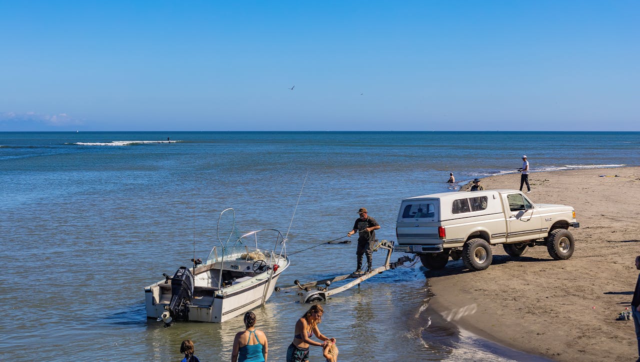 A relaxing day at the beach with a jeep towing a boat and people enjoying the sunshine.